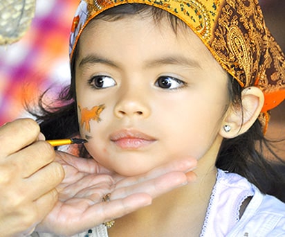 little girl with a yellow bandana getting a tiger painted on her face at a farm